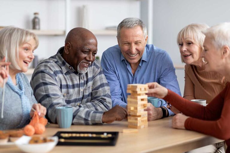 An elderly resident sits in a sunlit lounge exchanging stories with peers, surrounded by comfortable furniture and greenery.