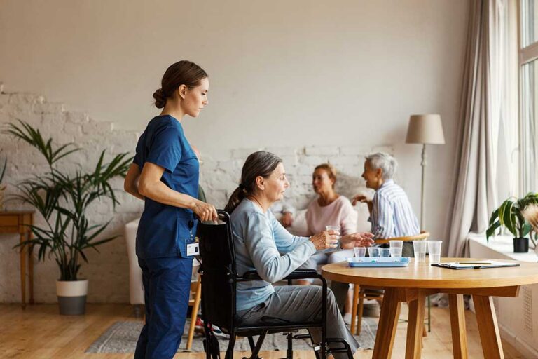 Older adult walking with a walker beside a caregiver in a bright assisted living hallway.