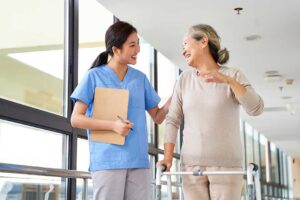 Caregiver sanitizes hands beside an older resident in a bright assisted living common room.